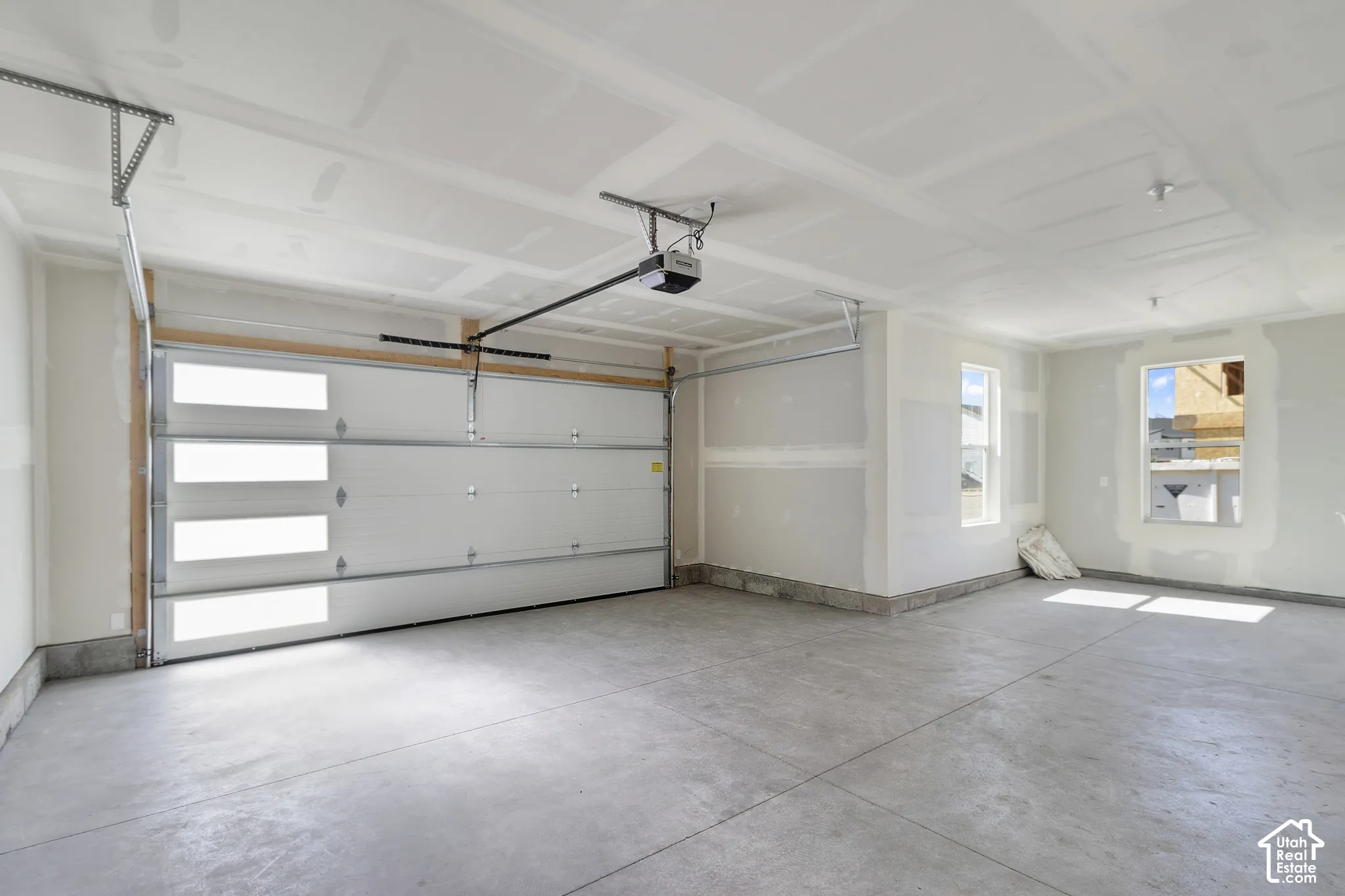 Concrete flooring, two windows, automatic garage door opener, white paneled garage door with horizontal glass inserts, interior walls with drywall