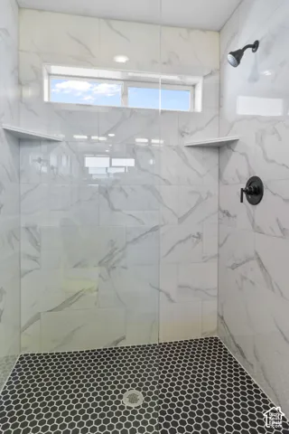Walk-in shower with large format wall tiles, black hexagonal floor tiles, and a transom window