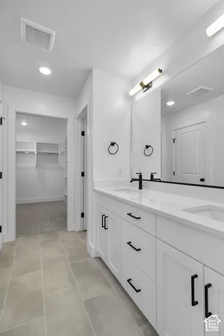 Dual vanity with white cabinetry and quartz countertops, matte black plumbing fixtures, large framed mirror, and tiled flooring