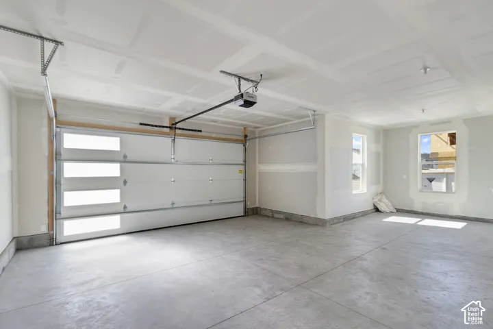 Concrete flooring, two windows, automatic garage door opener, white paneled garage door with horizontal glass inserts, interior walls with drywall