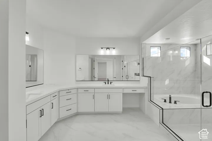 Dual vanity with white cabinetry, built-in makeup vanity, large soaking tub, and enclosed glass shower
