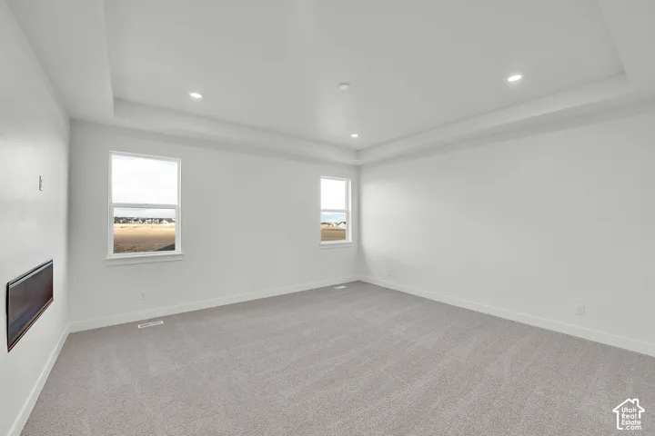 Tray ceiling with recessed lighting, light-colored carpeting, multiple windows, and a built-in electric fireplace