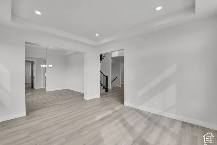 Tray ceiling, recessed lighting, wood-finish flooring, white walls, and a staircase with black railings