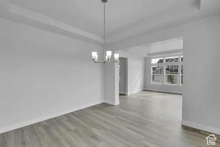 Recessed ceiling with a contemporary chandelier, wood-finish flooring, and large windows