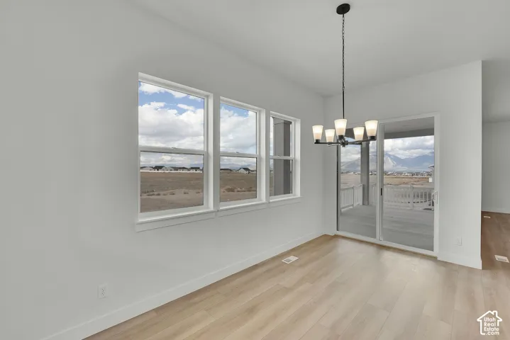 Light-toned wood-finish flooring, three large windows with white trim, a sliding glass door, and a black chandelier with five white glass shades