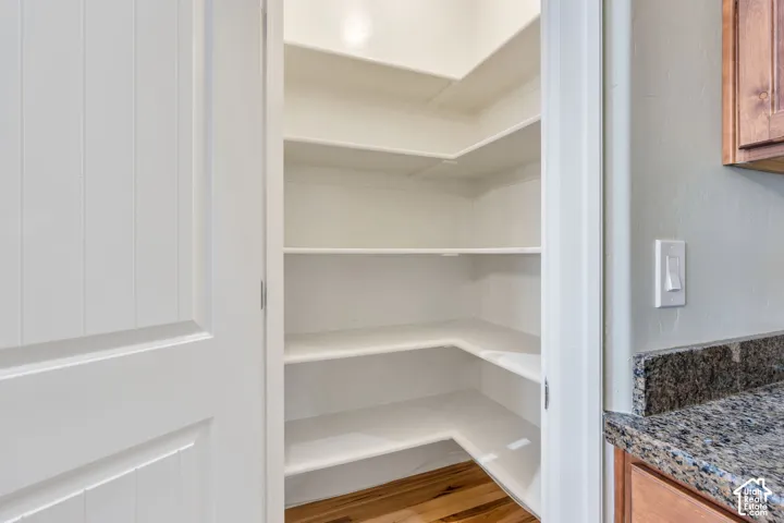 Walk-in pantry featuring multiple white shelves and wood-finish flooring
