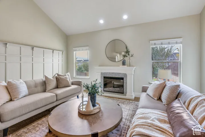 Vaulted ceiling, decorative wall paneling,  fireplace, recessed lighting, and large windows providing natural light.
