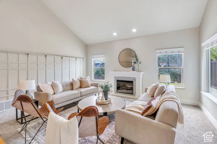 Vaulted ceiling, decorative wall paneling,  fireplace, recessed lighting, and large windows providing natural light.