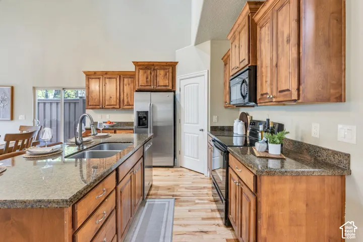 Open concept living space featuring vaulted ceilings, wood-finish flooring, kitchen island with built-in sink, stainless steel appliances, and updated light fixtures and updated chandelier. Wood cabinets and granite countertops