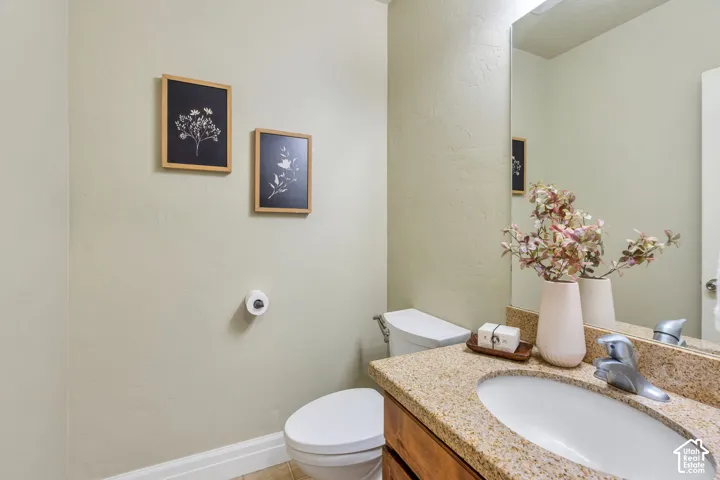 main level half bath with vanity, a polished stone countertop, undermount sink, and chrome faucet and updated vanity light fixture
