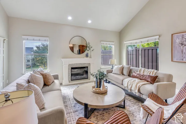 Vaulted ceiling, decorative wall paneling,  fireplace, recessed lighting, and large windows providing natural light.