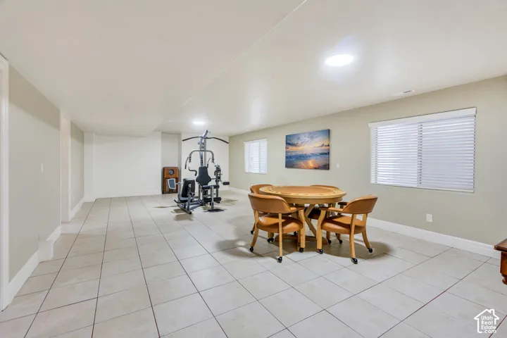 Spacious home gym or game room featuring light-colored floor tiling, recessed lighting, and multiple windows with blinds