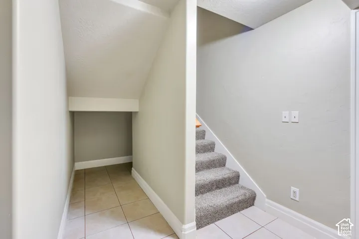 Carpeted stairs with tile flooring and a recessed under-stair area that could be used for storage or a kids playroom.