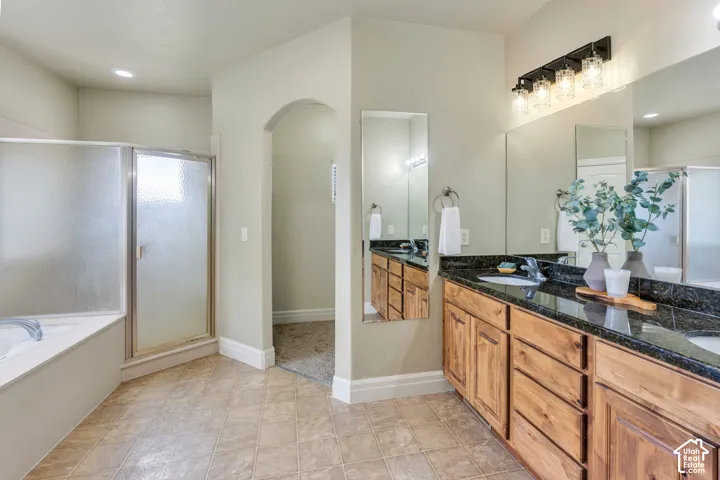 Main level primary bathroom features a double sink vanity with wood cabinetry, a separate shower, a relaxing soaking tub, and an adjoining primary closet.