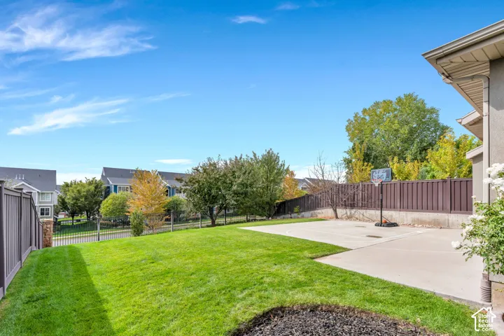 Expansive outdoor space featuring a manicured lawn, concrete patio, a fence, mature trees, and a sport court.