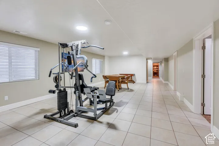 Spacious home gym or game room featuring light-colored floor tiling, recessed lighting, and multiple windows with blinds