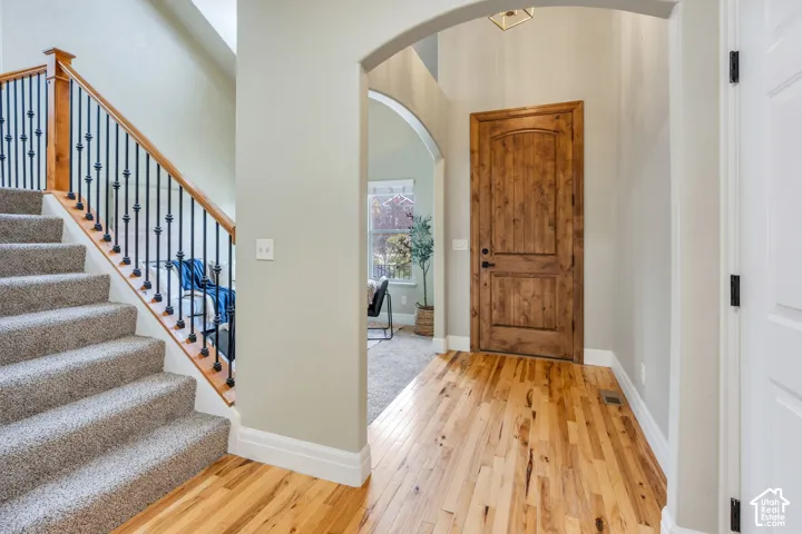 Hardwood-style flooring, arched entryway, Solid wood door with updated black hardware, carpeted staircase, and decorative wrought iron balusters