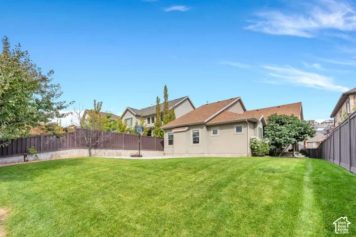 Expansive backyard featuring a manicured lawn, established trees, and a durable vinyl privacy fence, a sport court, a garden and a beautiful Fig Tree.
