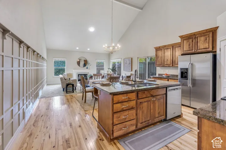 Open concept living space featuring vaulted ceilings, wood-finish flooring, kitchen island with built-in sink, stainless steel appliances, and updated light fixtures and updated chandelier. Wood cabinets and granite countertops