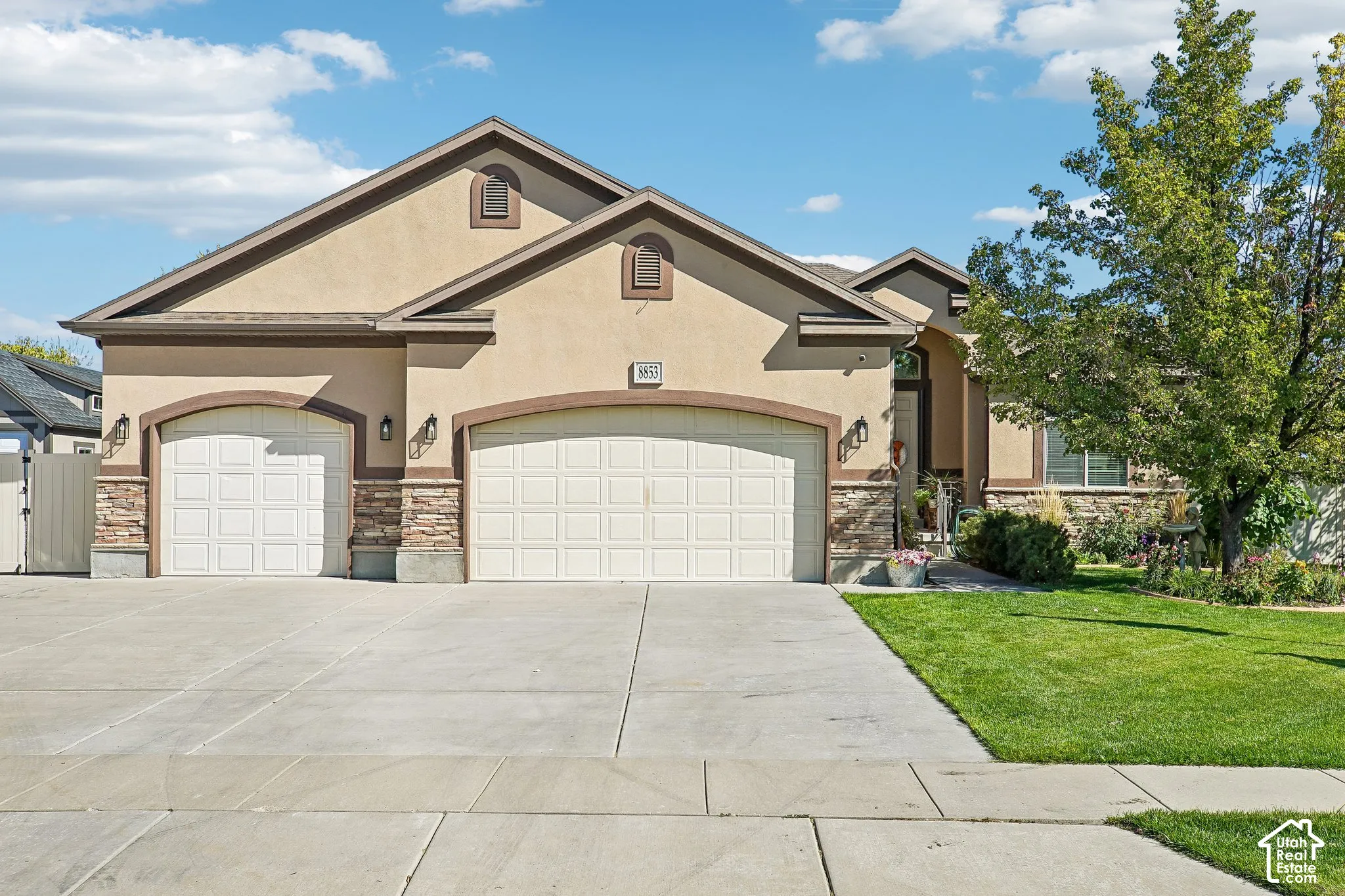 Stucco exterior with stone accents, multiple garage doors, concrete driveway, and a landscaped front yard with mature trees
