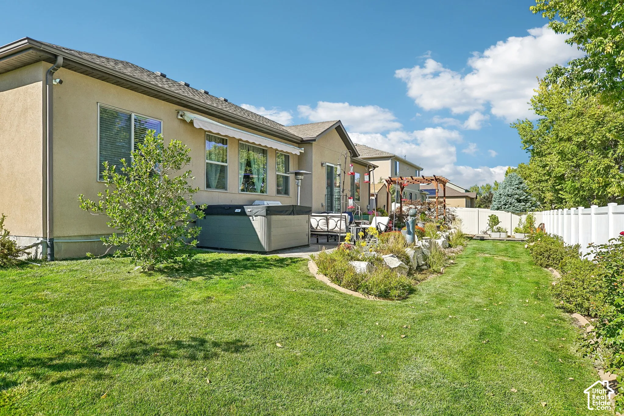 Expansive backyard featuring a stucco exterior, multiple windows, a retractable awning, and a privacy fence