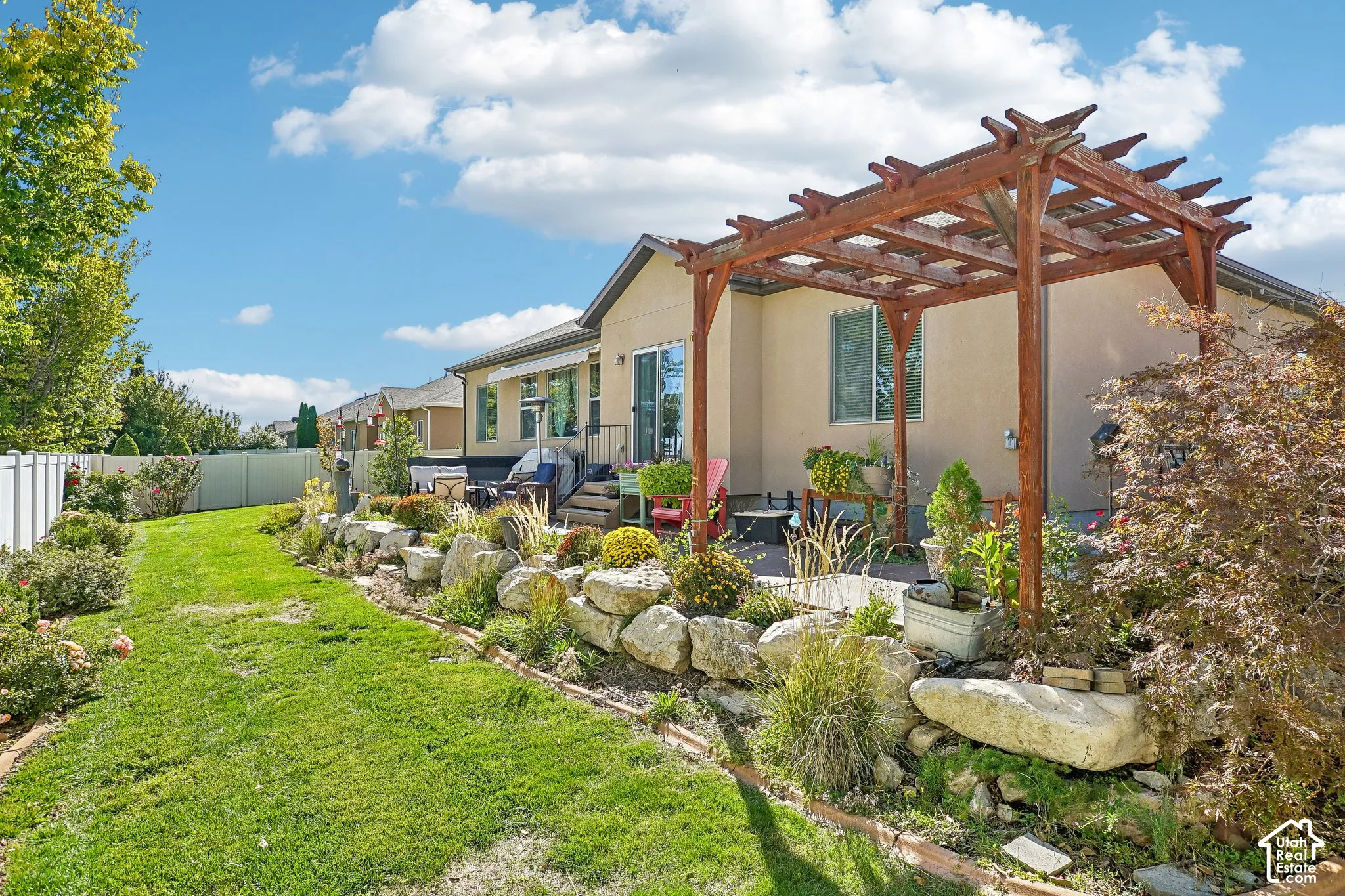 Expansive backyard featuring a manicured lawn, a white privacy fence, an elevated patio with a wooden pergola, and a rock garden with established plantings