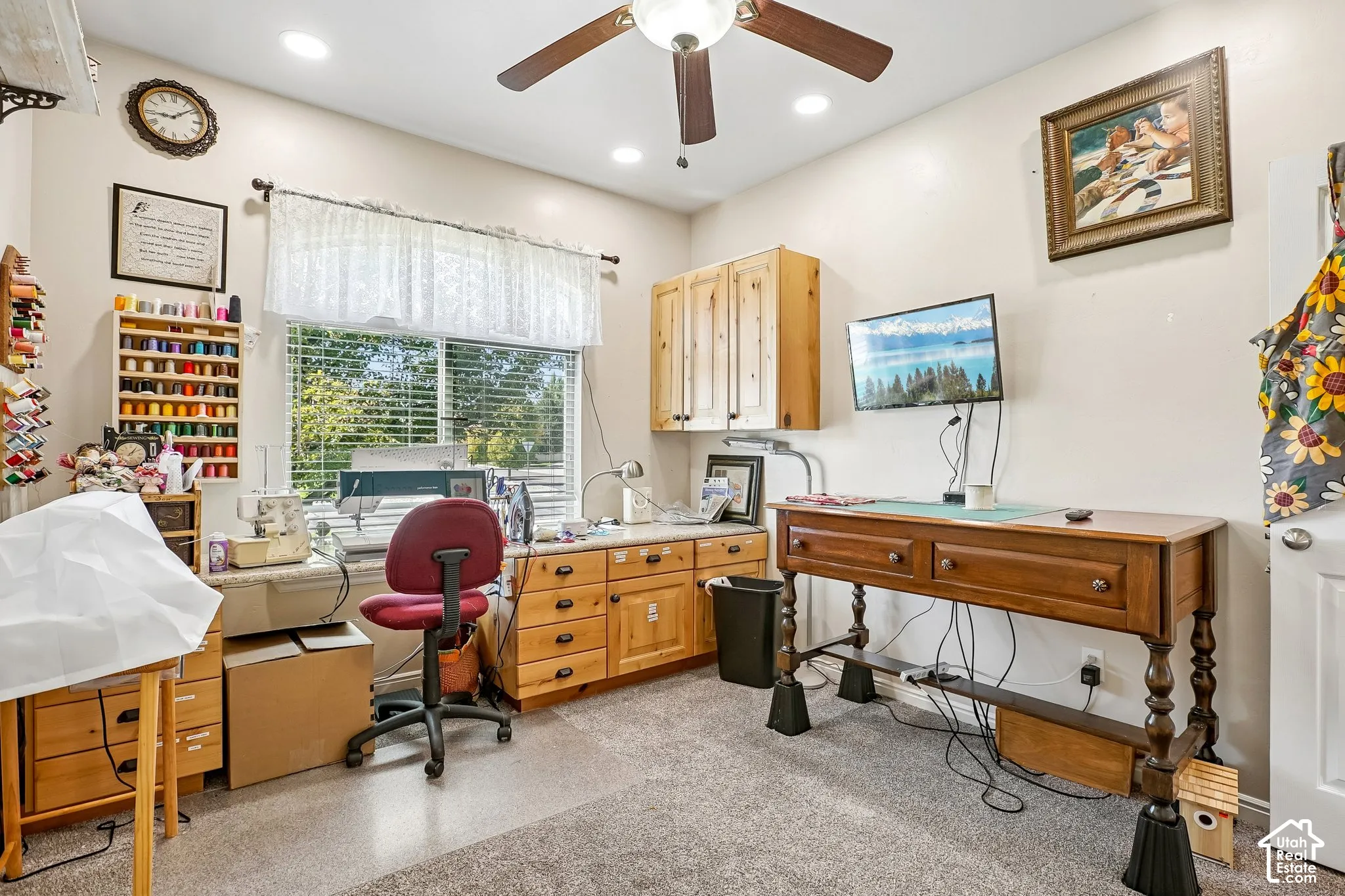 Recessed lighting and a ceiling fan illuminate the space, which features wood-finish cabinetry, a large window, and light-colored carpeting