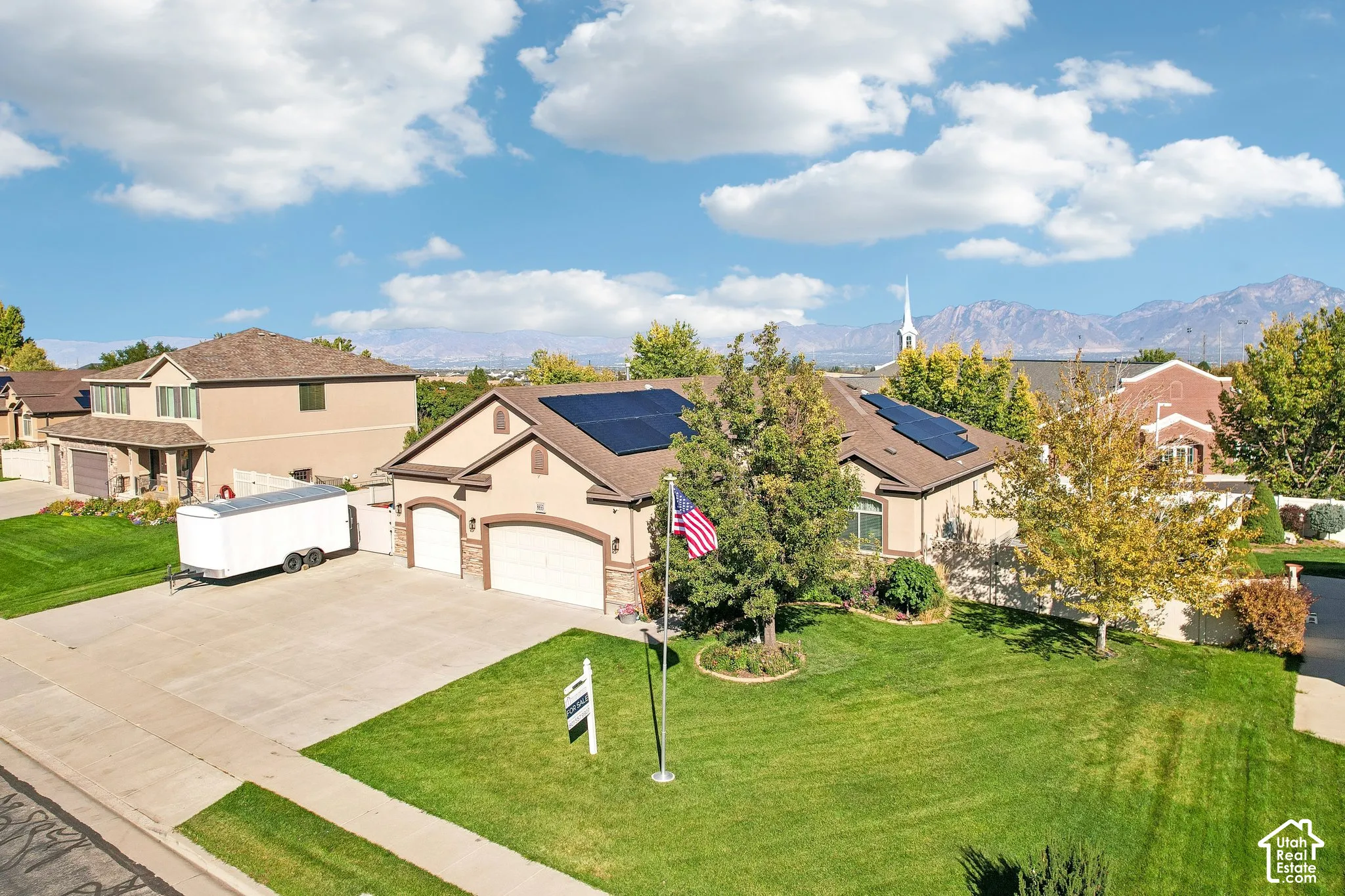 Single-story residence featuring a two-car garage with arched entrances, mature front yard landscaping, solar panels, and a prominent mountain backdrop