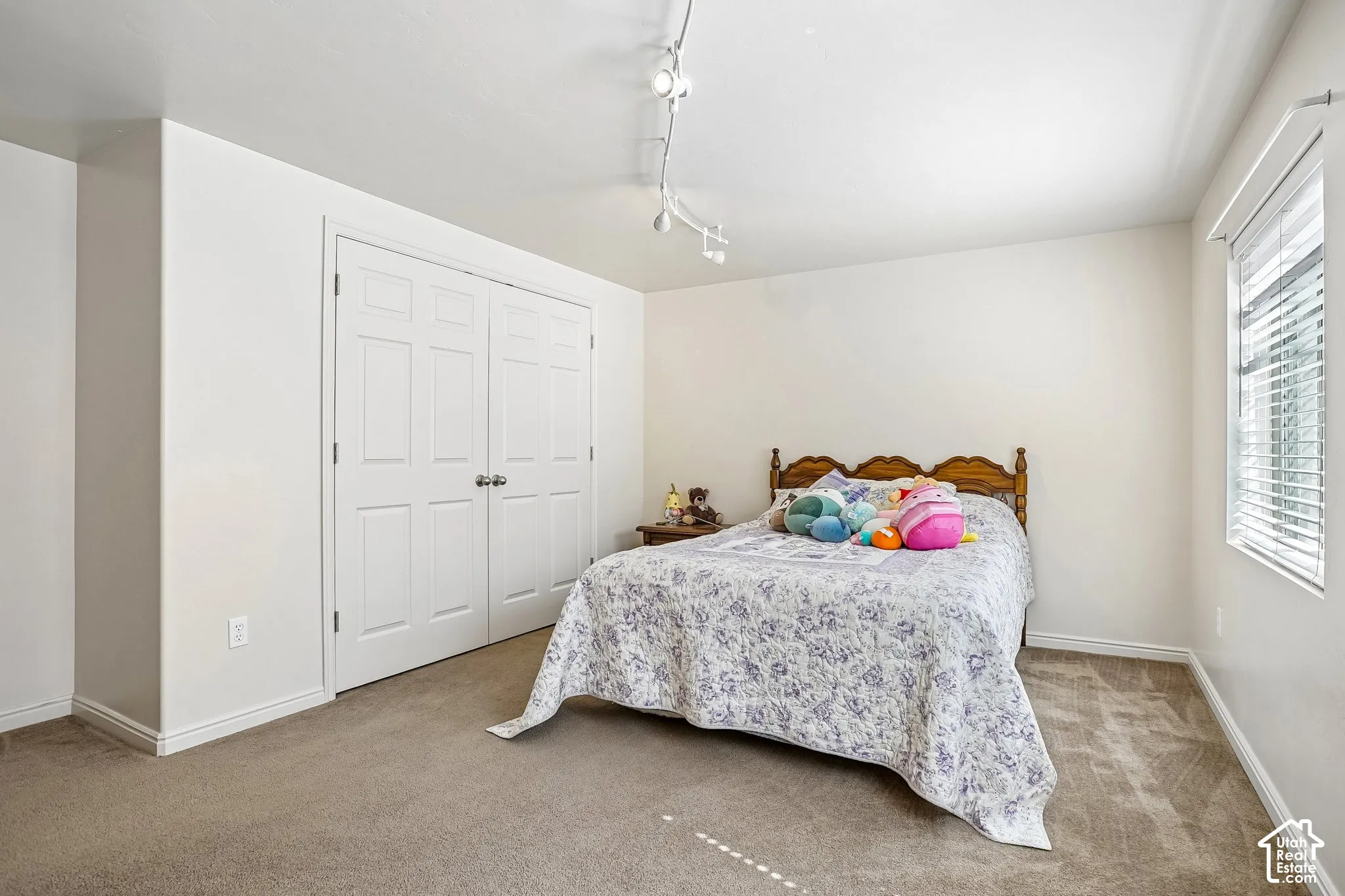 Light-filled room featuring neutral wall tones, warm carpet flooring, a window with horizontal blinds, and a built-in closet with paneled bifold doors