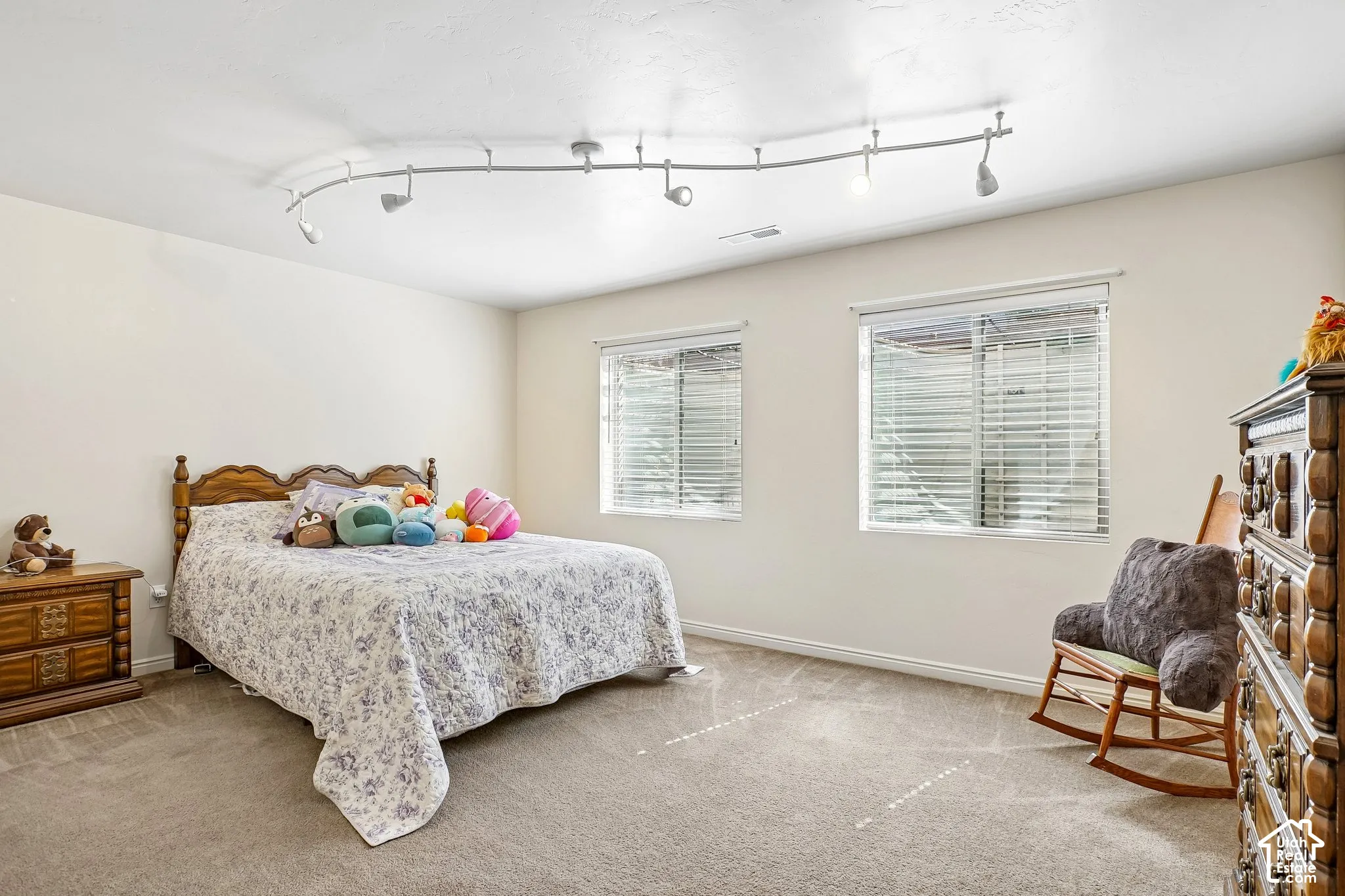 Neutral wall color, wall-to-wall carpeting, two windows with blinds, and track lighting