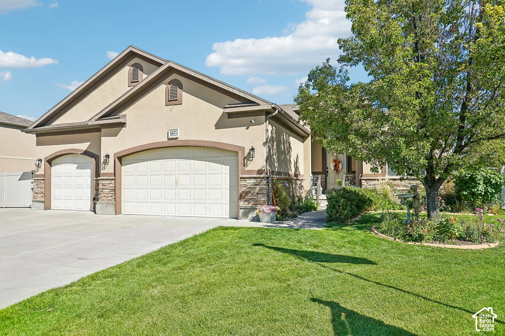Stucco exterior with stone accents, two-car garage, manicured lawn, established landscaping, and concrete driveway