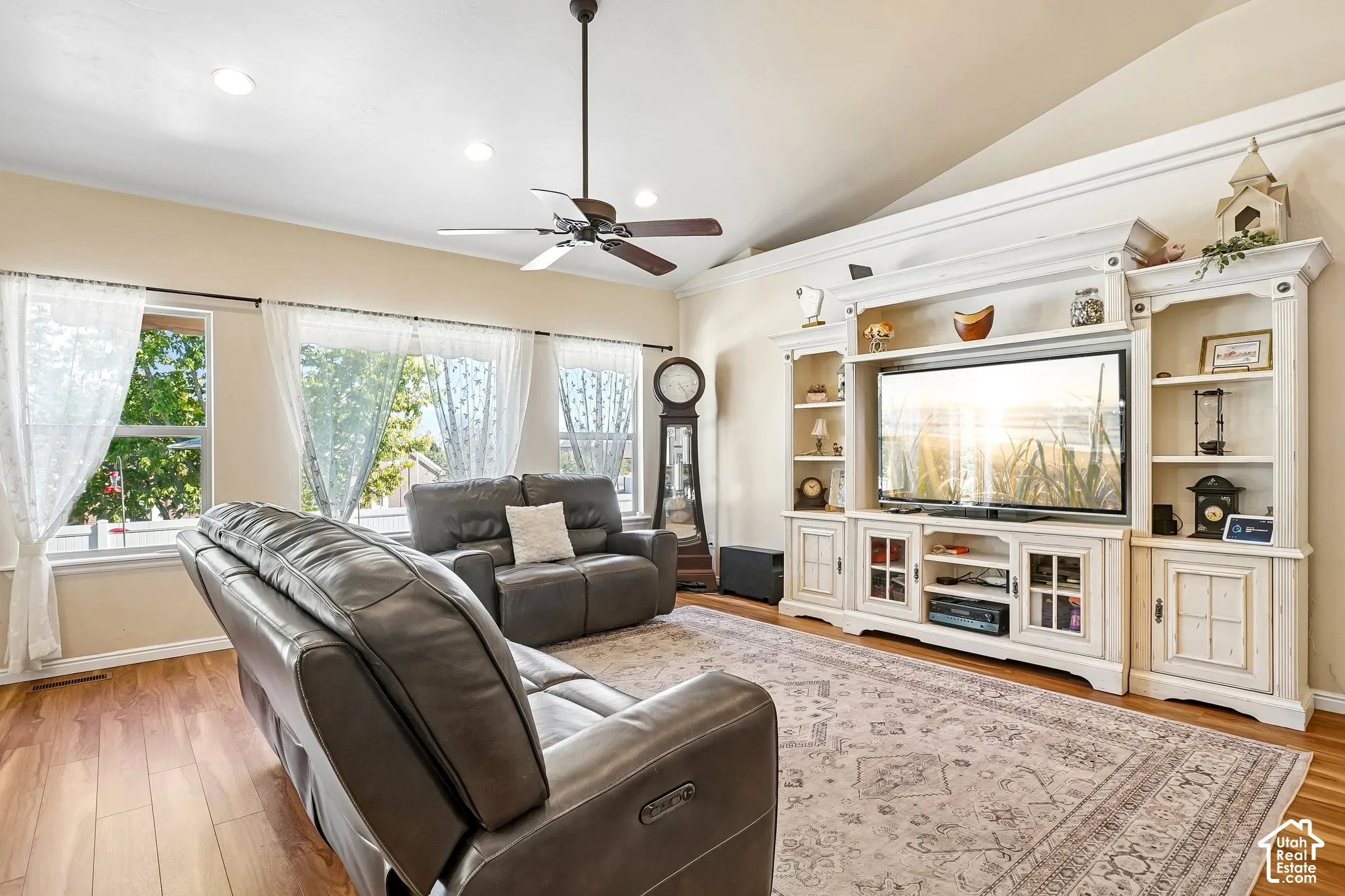 Vaulted ceiling with recessed lighting, wood-finish flooring, multiple windows, built-in entertainment center, and a ceiling fan