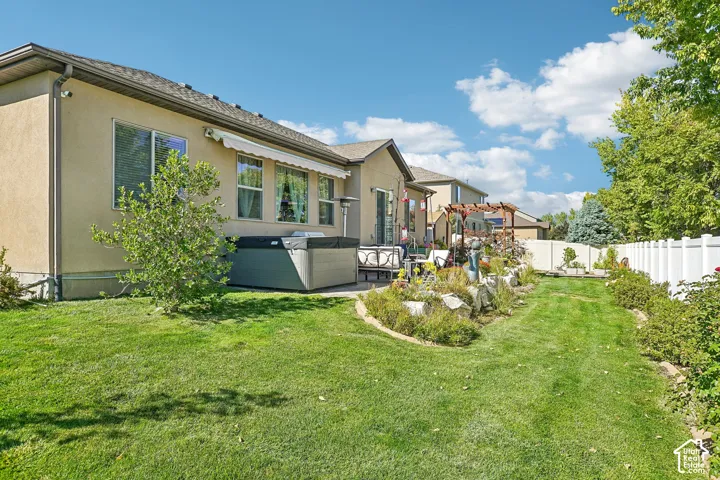 Expansive backyard featuring a stucco exterior, multiple windows, a retractable awning, and a privacy fence