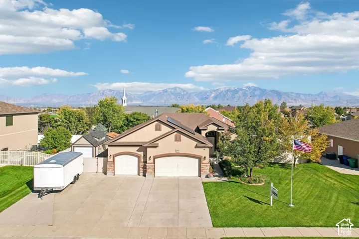 Expansive concrete driveway, two-car garage, manicured lawn with mature trees, and a detached shed
