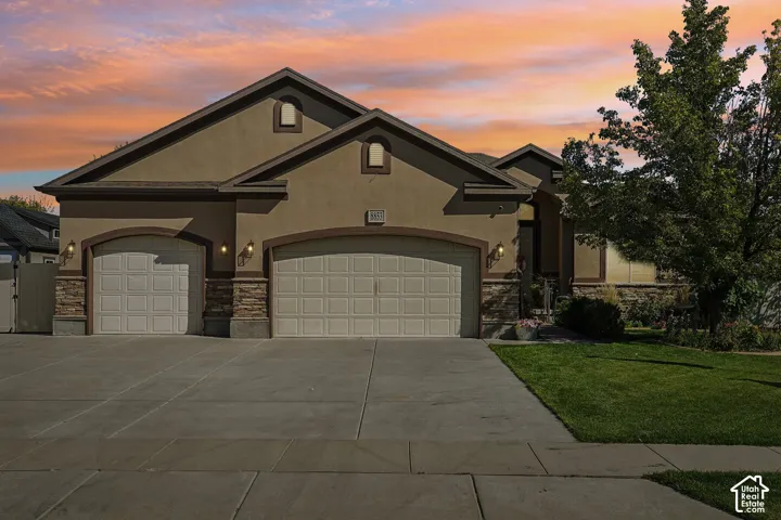 Stucco exterior with stone accents, dual arched garage doors, a concrete driveway, and a landscaped front yard