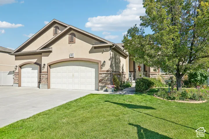 Stucco exterior with stone accents, two-car garage, manicured lawn, established landscaping, and concrete driveway
