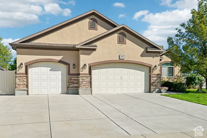 Stucco exterior with stone accents, two arched garage doors, and carriage-style outdoor lighting