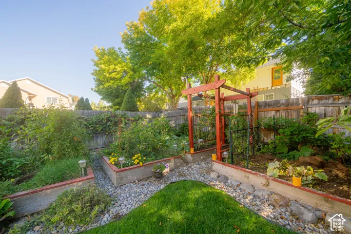 Expansive backyard featuring raised garden beds, a gravel pathway, and a wooden arbor
