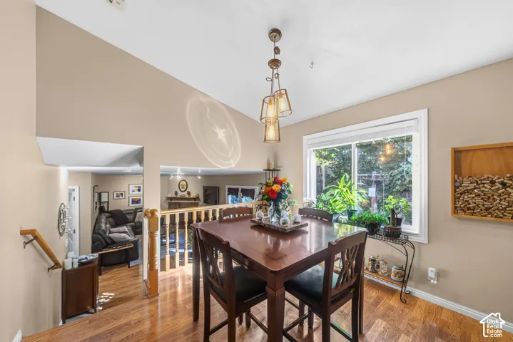 Vaulted ceilings, wood-finish flooring, a large window, a decorative hanging light fixture, and a wood railing