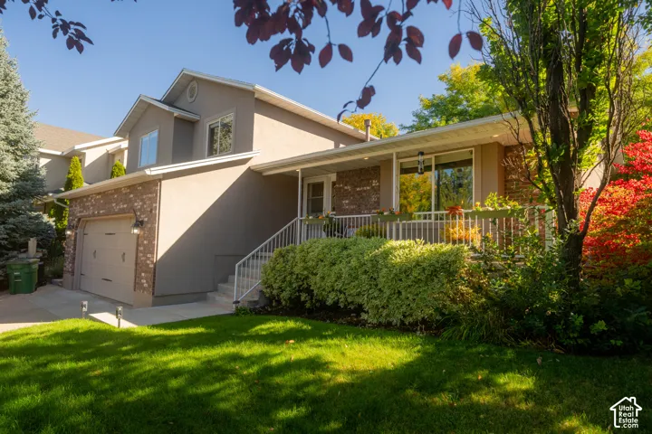 Stucco and brick facade with a built-in garage, front porch with white railing, and exterior lighting fixtures