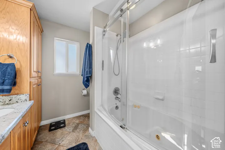 White bathtub with sliding glass doors, chrome fixtures, and a multi-bulb light fixture