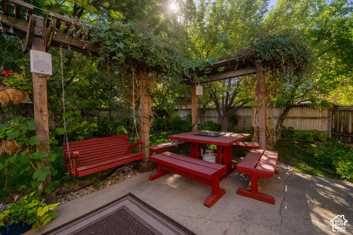 Patio area featuring a wooden pergola with mature vines, concrete ground surface, and a wooden fence