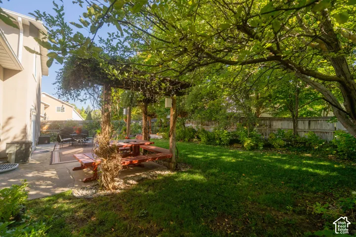 Expansive grassy yard with mature trees, wooden fence, and a concrete patio