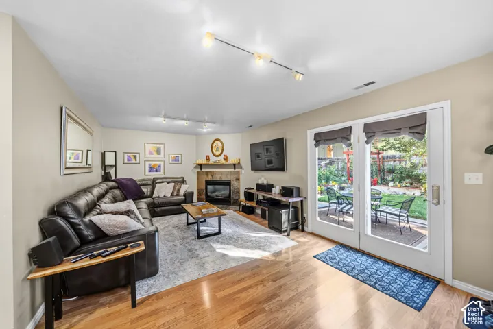 Hardwood flooring, fireplace with stone surround, track lighting, and double glass doors opening to a fenced backyard