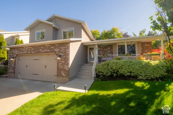 Stucco and brick facade with an attached garage, covered front porch, and mature landscaping