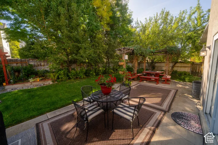 Expansive concrete patio with pergola, mature trees, and manicured lawn