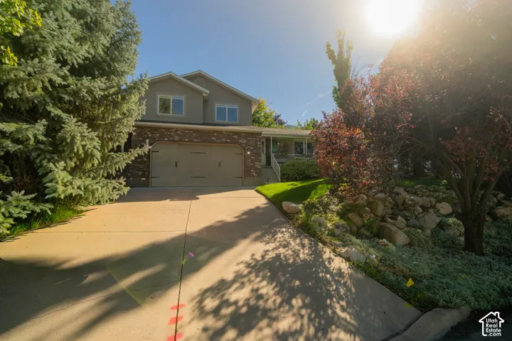 Two-story residence featuring a two-car garage, brick facade detailing, mature trees, and a concrete driveway