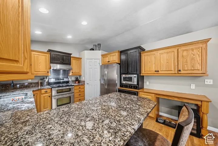 Kitchen featuring granite countertops, wood-finish cabinetry, stainless steel appliances, recessed lighting, and a built-in oven