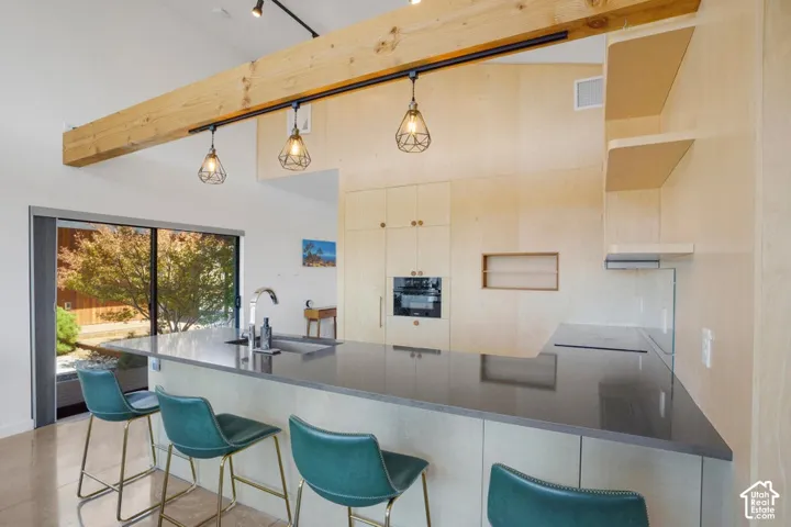 Vaulted ceiling with exposed timber beam, built-in track lighting, large sliding glass door, integrated wall oven, and built-in cabinetry