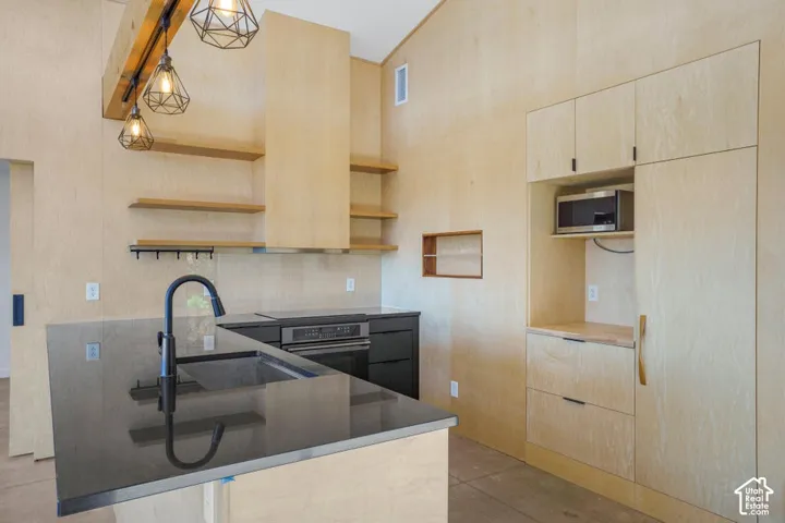 Vaulted ceilings with exposed beam, geometric pendant lighting, modern black faucet and undermount sink, built-in oven, and light wood-finish cabinetry